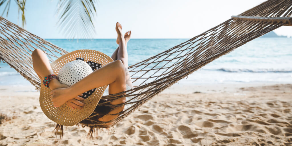 Titelbild FTI Group - Person entspannt sich in einer Hängematte am Strand mit Blick auf das Meer