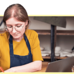 Keramikkünstlerin gestaltet ihren Online-Shop am Laptop in der Töpferwerkstatt