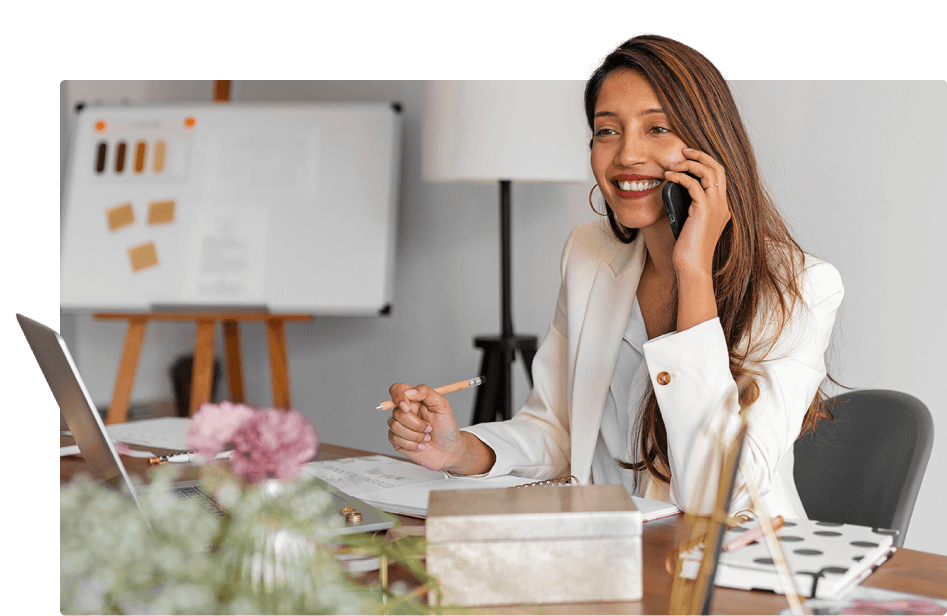 Eine lächelnde Frau im Büro spricht am Telefon, professionell gekleidet, in einer hellen, modernen Arbeitsumgebung.  