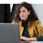 Eine Frau arbeitet konzentriert an einem Laptop, trägt Kopfhörer und eine gelbe Jacke.