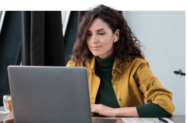 Eine Frau arbeitet konzentriert an einem Laptop, trägt Kopfhörer und eine gelbe Jacke.