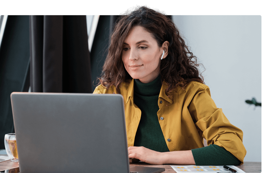 Eine Frau arbeitet konzentriert an einem Laptop, trägt Kopfhörer und eine gelbe Jacke.