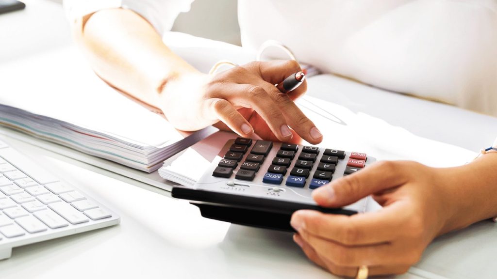 Nahaufnahme einer Person, die mit einem Taschenrechner arbeitet, während sie Zahlen berechnet und Notizen macht.