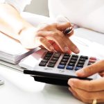 Nahaufnahme einer Person, die mit einem Taschenrechner arbeitet, während sie Zahlen berechnet und Notizen macht.