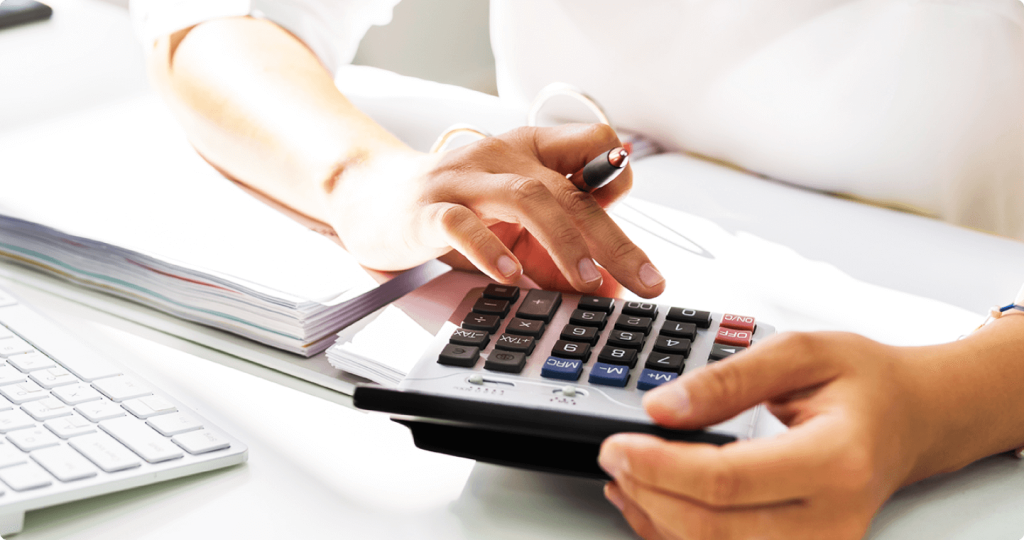 Nahaufnahme einer Person, die mit einem Taschenrechner arbeitet, während sie Zahlen berechnet und Notizen macht.