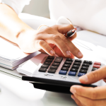 Nahaufnahme einer Person, die mit einem Taschenrechner arbeitet, während sie Zahlen berechnet und Notizen macht.