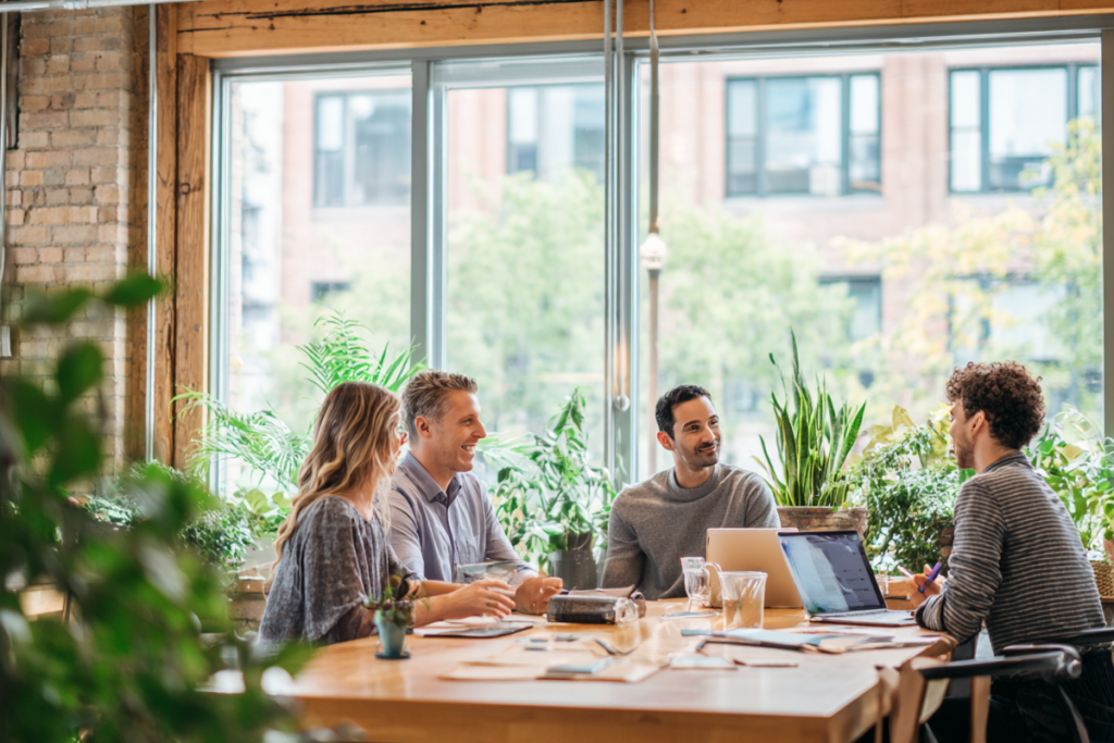 Team diskutiert an einem Laptop über elektronische Rechnungsstellung und EN 16931 in einem modernen Büro. Eine Person macht sich Notizen, während eine andere auf den Bildschirm zeigt, mit Kollegen im Hintergrund.