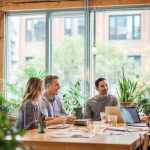 Team diskutiert an einem Laptop über elektronische Rechnungsstellung und EN 16931 in einem modernen Büro. Eine Person macht sich Notizen, während eine andere auf den Bildschirm zeigt, mit Kollegen im Hintergrund.